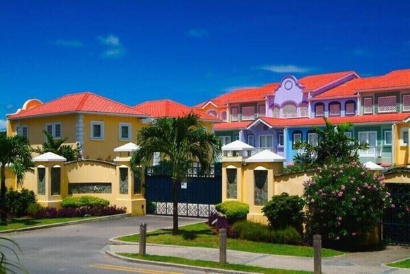 A row of colorful houses with red roofs, a gated entrance, and a clear blue sky. - Harbour 12 - 2 Bedroom (Gros Islet)