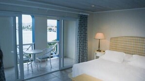 A hotel room with a bed, a nightstand, a lamp, a window, and a balcony with a table and chairs. - Harbour 12 - 2 Bedroom (Gros Islet)
