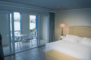 Ein Hotelzimmer mit Bett, Nachttisch, Lampe, Fenster und Balkon mit Tisch und Stühlen.
