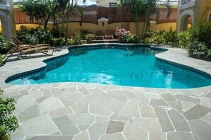 Una piscina con borde de piedra, rodeada de plantas y una valla de madera.