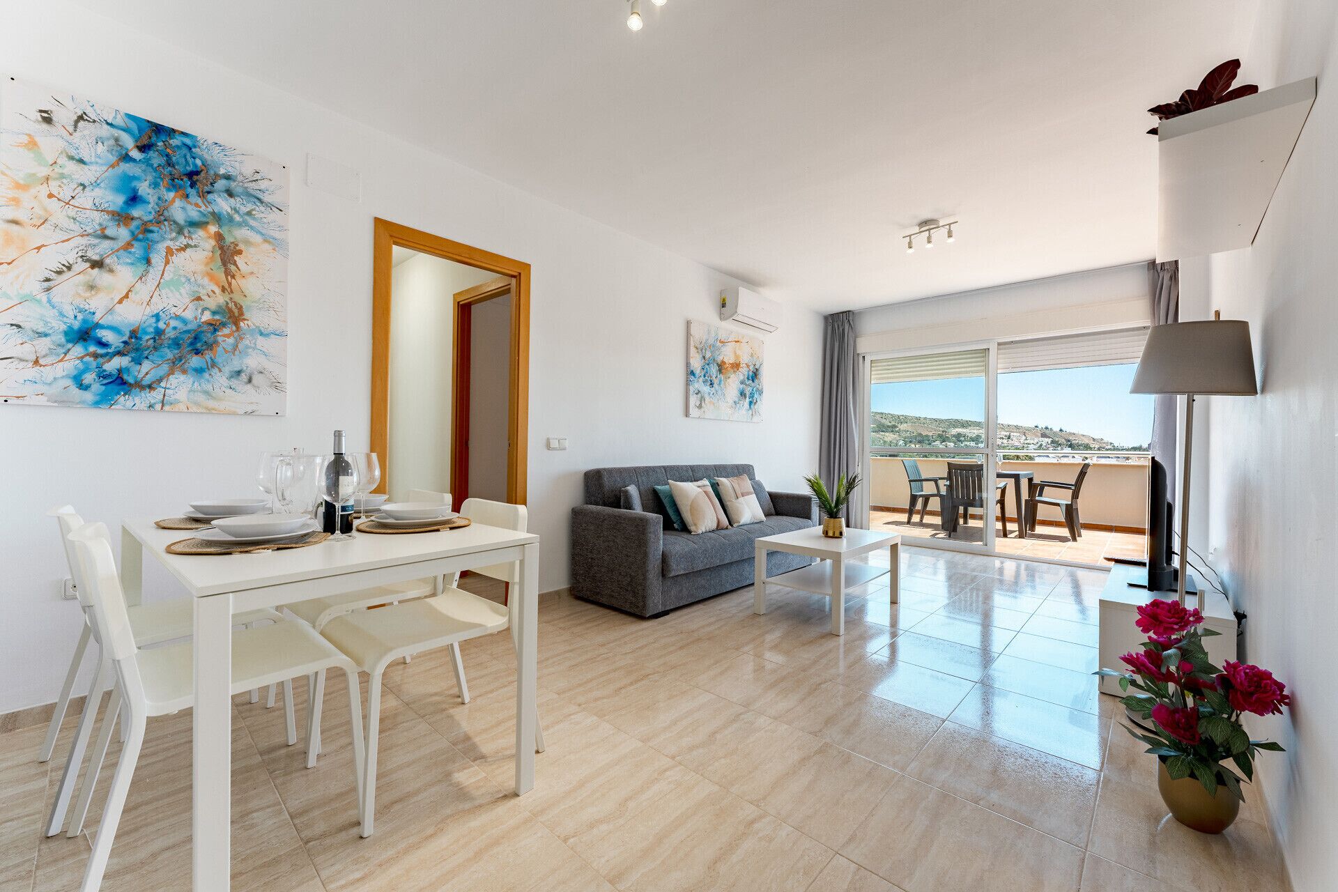 Un salon moderne comprenant un coin repas, un canapé gris, une table basse et un balcon avec vue.