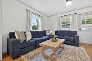 A living room with a sectional sofa, a wooden coffee table, and patterned rugs.