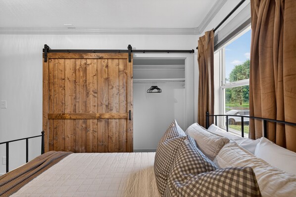 A bedroom with a bed, a wooden sliding door, a window with curtains, and a hanging coat rack.