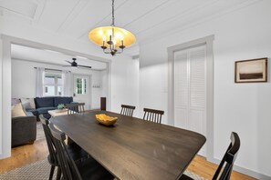 A dining area with a wooden table, chairs, a chandelier, and a view to a living room. - Cozy Crane Cottage, WestGate~3 Bedroom 2 Bathroom~ (Crane)
