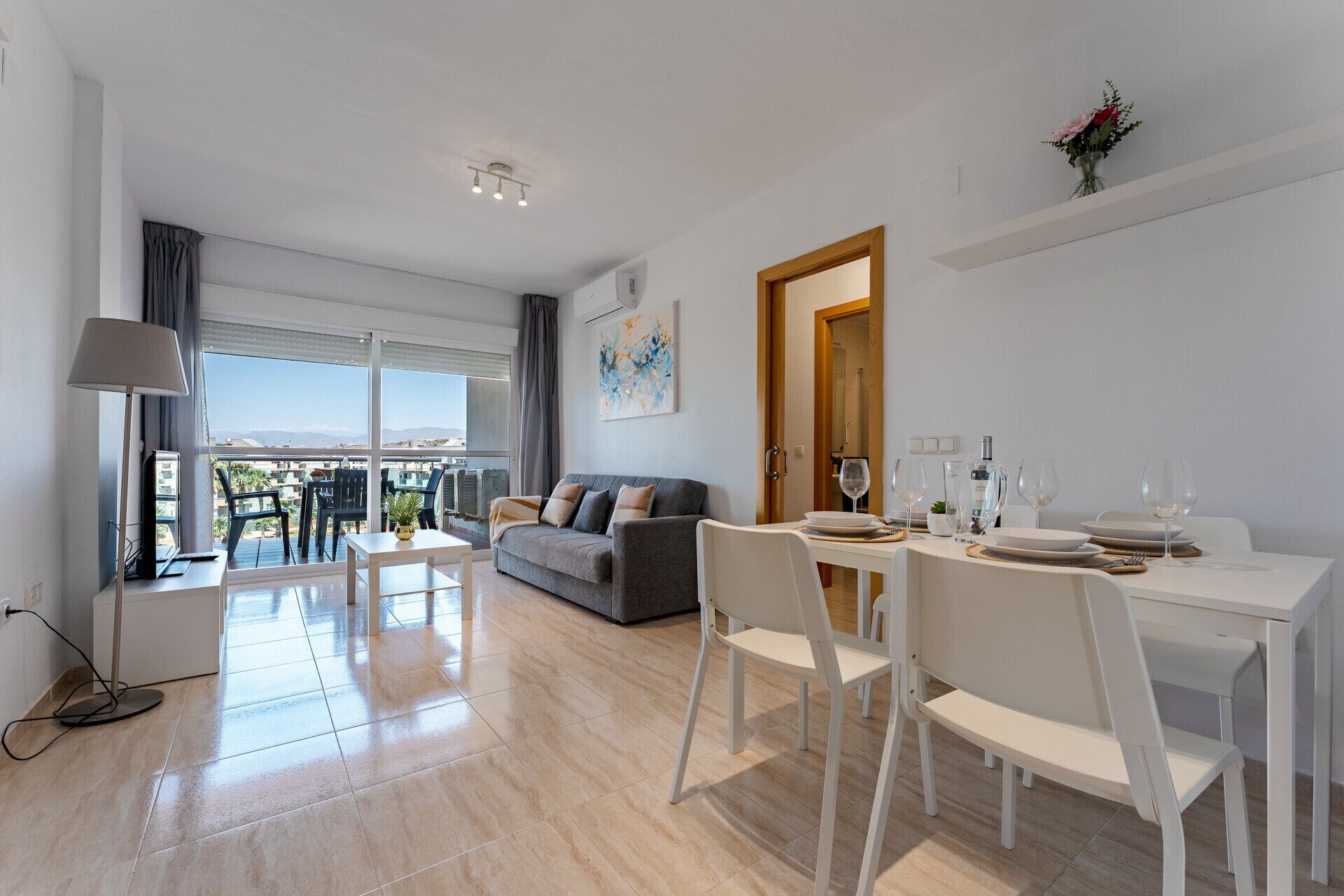 Un salon moderne avec un canapé, une table à manger et des chaises, un balcon avec vue et un tableau accroché au mur.