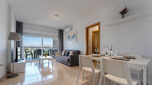Un salon moderne avec un canapé, une table à manger et des chaises, un balcon avec vue et un tableau accroché au mur.