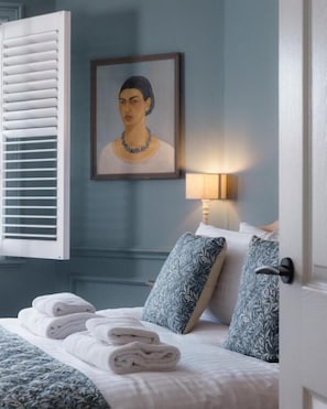 A neatly made bed with rolled towels, a framed portrait on the wall, and a bedside lamp.