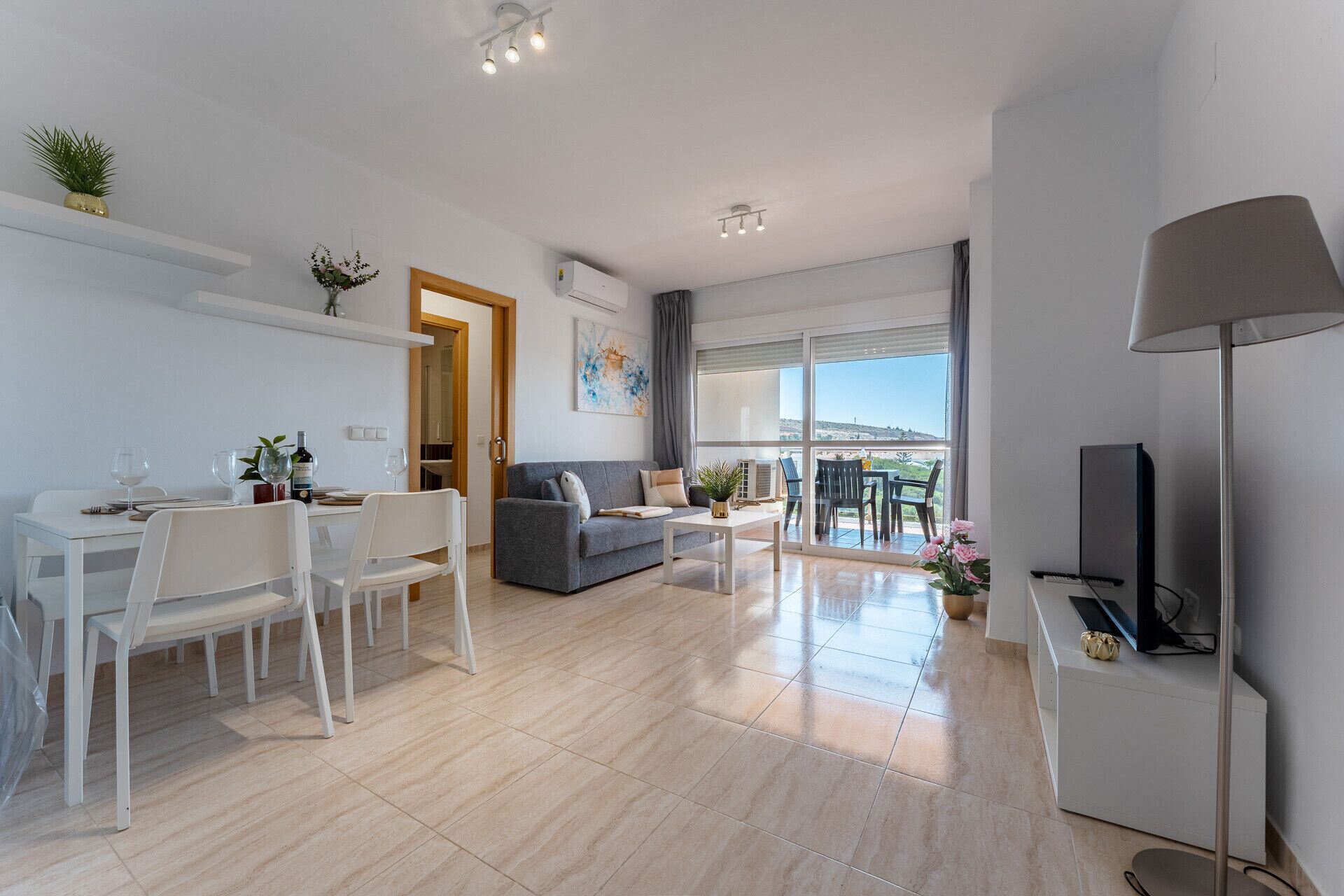 Een moderne woonkamer met een eethoek, een grijze bank, een televisie en een balkon met uitzicht.