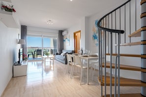 Eine moderne Wohnung mit Essbereich, einer Couch, einer Treppe und Blick durch große Fenster.