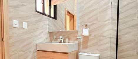 A modern bathroom with a marble floor, a wooden vanity, a white toilet, and a glass shower enclosure.