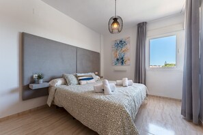 Une chambre à coucher moderne avec un lit, une table de chevet, un luminaire suspendu, une fenêtre avec des rideaux et un tableau au mur.
