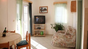 Uma sala de estar com televisão, sofá, mesa de jantar com cadeiras e um vaso de planta.
