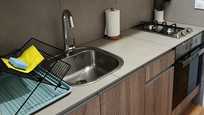 Een keuken met een roestvrijstalen spoelbak, een gasfornuis, houten kastjes en een afwassigheid met schoonmaakmiddelen.