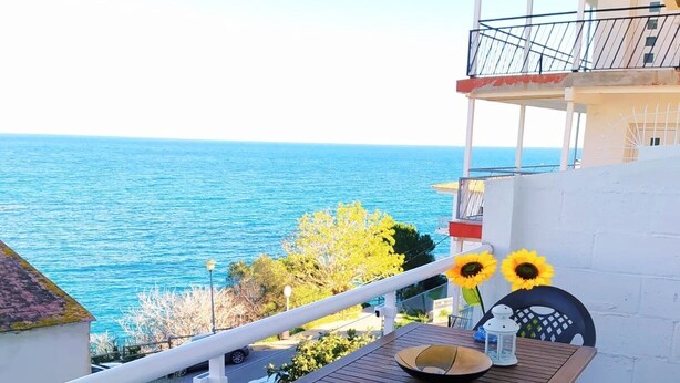 Een balkon met een tafel, stoelen en zonnebloemen, met uitzicht op een waterpartij.