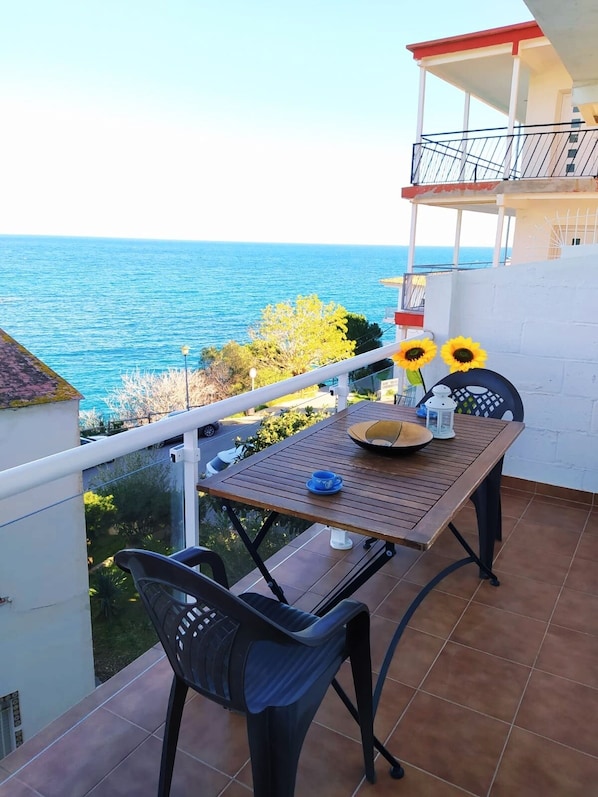 Ein Balkon mit Tisch, Stühlen und Sonnenblumen mit Blick auf ein Gewässer.