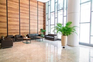 Eine geräumige Lobby mit hoher Decke, großen Fenstern und einer zentralen Sitzecke mit Sofas und Tischen.