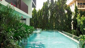 A swimming pool surrounded by greenery, with modern buildings in the background. - Solaris Premier 1BR | Osu • Pool • Gym (Accra)