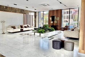 A spacious lobby with a modern sofa, a coffee table with plants, and a large window offering a view of the outside. - Harmonia Studio | Airport City • Pool • Fast WiFi (Accra)
