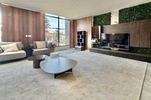 A modern living room with a large TV, a sofa, a coffee table, and a green wall. - Harmonia Studio | Airport City • Pool • Fast WiFi (Accra)