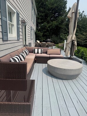 Eine Terrasse mit einer braunen Rattan-Couch, einem runden Hocker und einem Esstisch mit Stühlen.