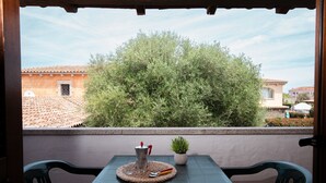 Un balcon avec une table, des chaises, une cafetière, une petite plante en pot et une vue sur des immeubles et des arbres.