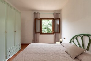 Ein Schlafzimmer mit einem Bett, einem Kleiderschrank, einem Fenster mit Vorhängen, einer Nachttischlampe und einem grünen Kopfteil.