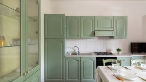 Une cuisine avec des meubles de couleur verte, un plan de travail recouvert de carreaux blancs, une cuisinière et une table à manger pour quatre personnes.