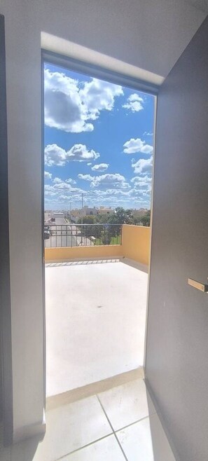 Blick von einem Balkon mit blauem Himmel und Wolken, einem Kachelboden und einem Metallgeländer.
