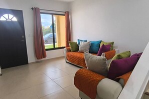 Ein Zimmer mit zwei Sofas, einem fensterbelaubten Fenster, einer Tür und Blick ins Freie.