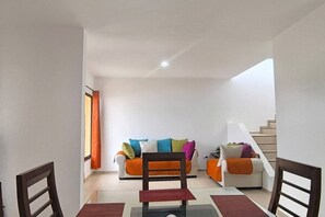 Ein Wohnzimmer mit einer Sofagarnitur, einem Esstisch und einer Treppe.
