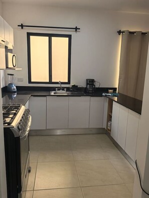 Una cocina moderna con armarios blancos, una estufa, una ventana con persianas y una cafetera.