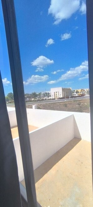 Blick durch ein Fenster auf einen wolkenlosen Himmel, ein weißes Gebäude und eine gepflasterte Fläche.