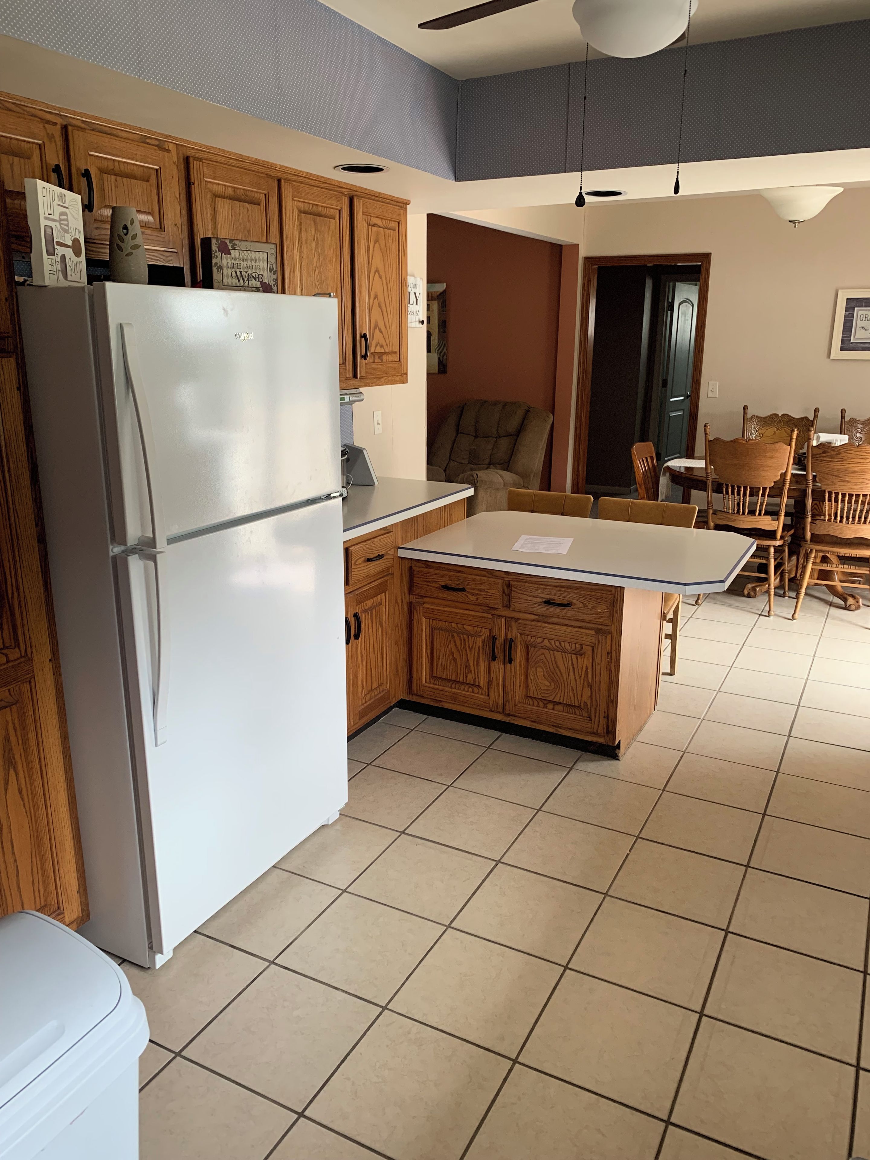 A kitchen with wooden cabinets, a white refrigerator, and a dining area with wooden chairs and a table.