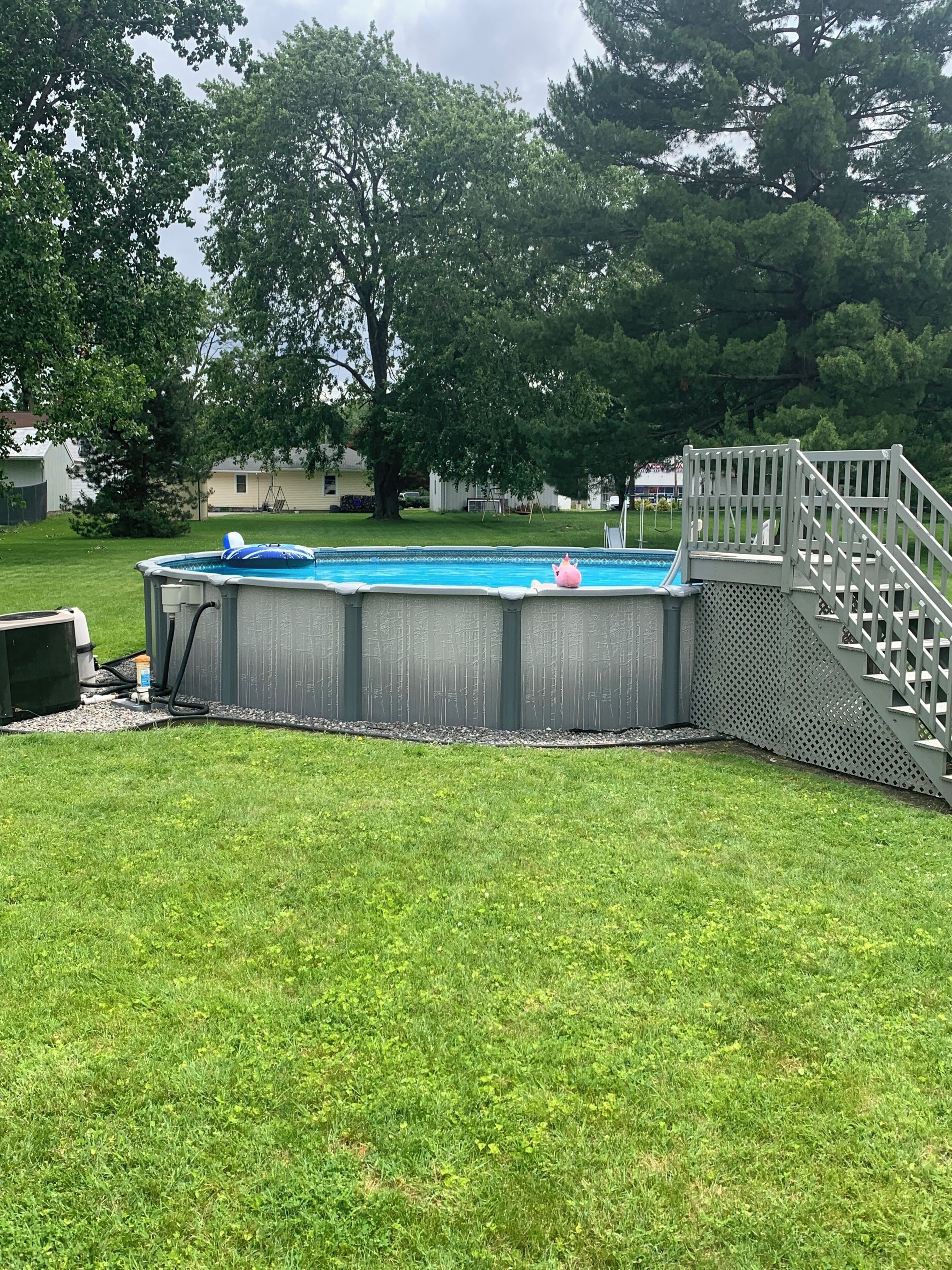 A backyard with a swimming pool, a wooden deck, and a grassy lawn.