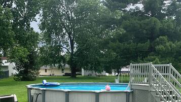 A backyard with a swimming pool, a wooden deck, and a grassy lawn.
