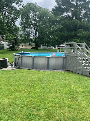 Un patio trasero con piscina, una terraza de madera y un césped.