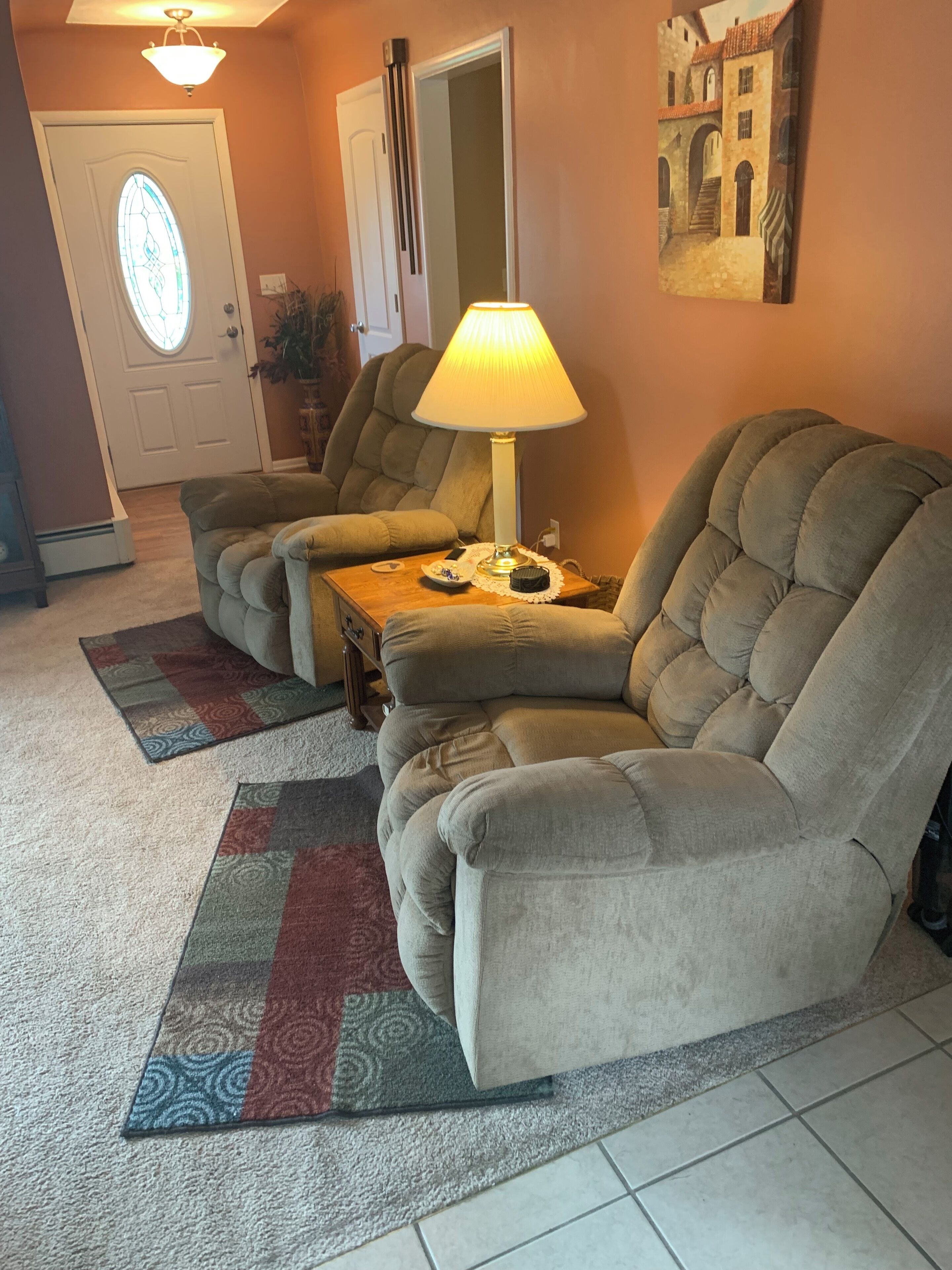 A living room with two beige armchairs, a wooden coffee table, a floor lamp, a patterned rug, and a painting on the wall.