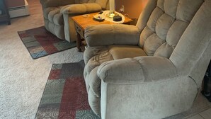 Een woonkamer met twee beige fauteuils, een houten salontafel, een vloerlamp, een kamerbreed tapijt met dessin en een schilderij aan de muur.