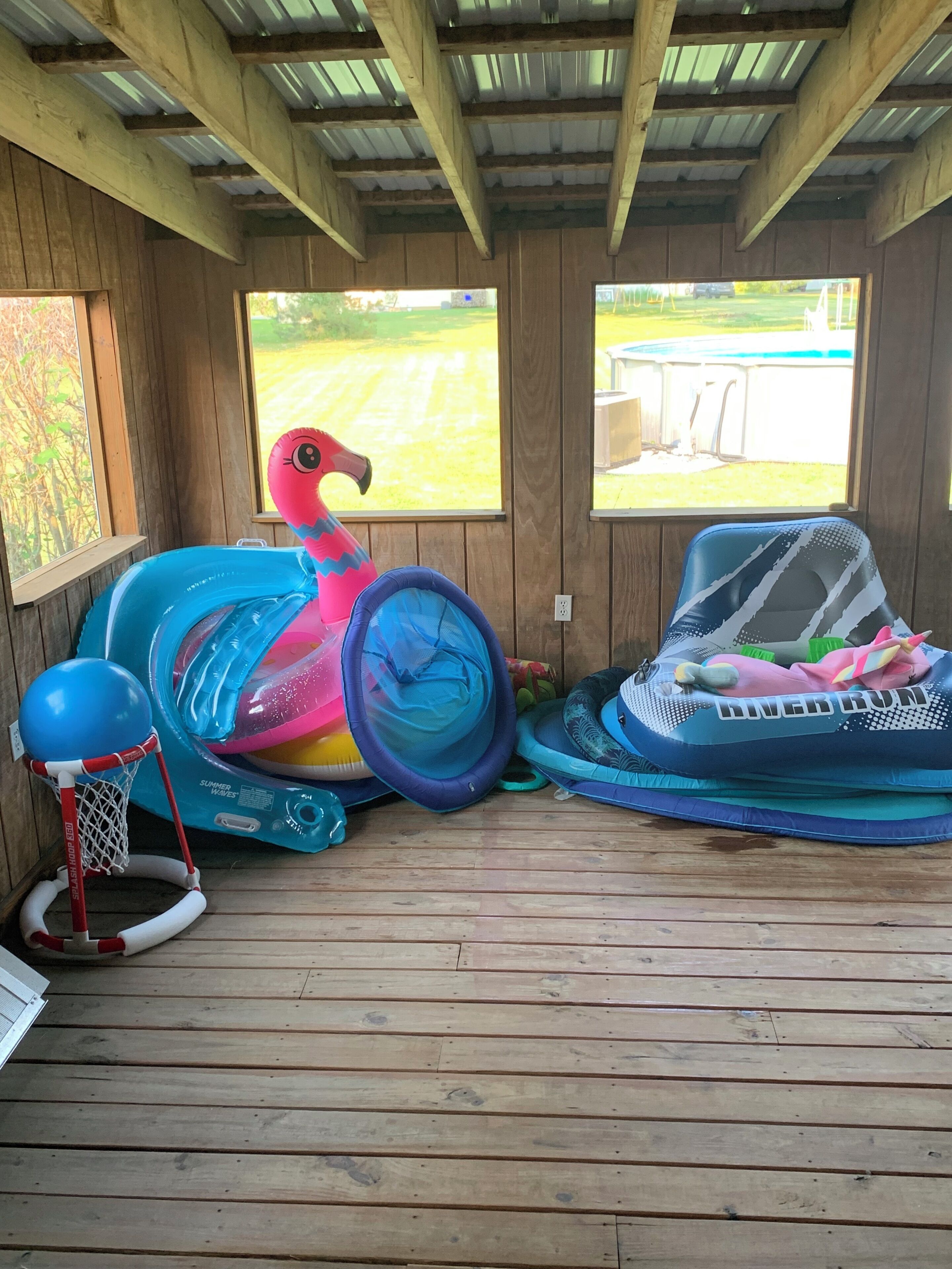 En överbyggd träveranda med uppblåsbara leksaker, bland annat en flamingo och en basketkorg.