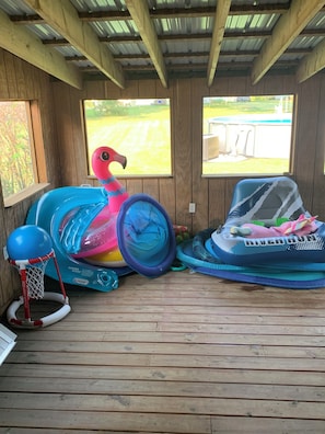 A covered wooden deck with inflatable play equipment, including a flamingo and a basketball hoop.