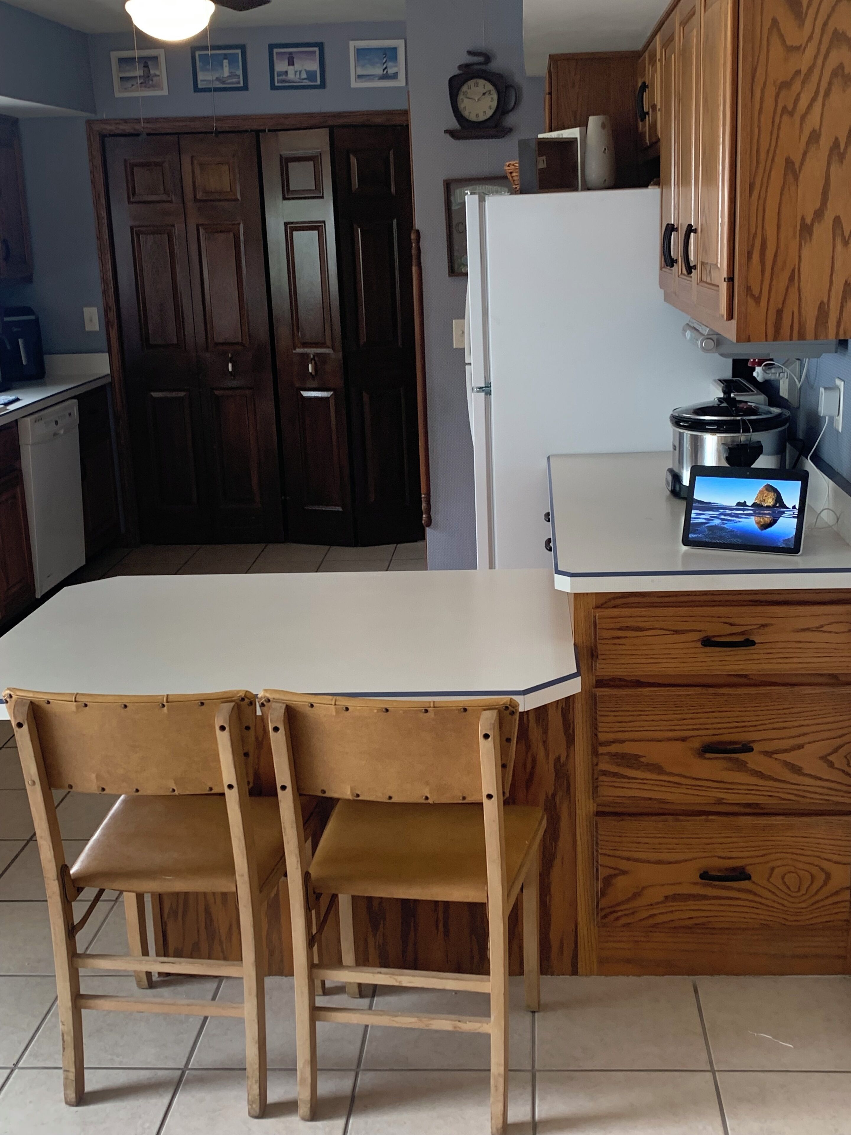 A kitchen with a dining table and chairs, a refrigerator, wooden cabinets, and a clock on the wall.