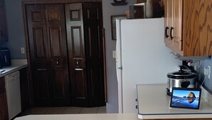 Een keuken met een eettafel en stoelen, een koelkast, houten kastjes en een klok aan de muur.