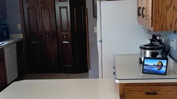 A kitchen with a dining table and chairs, a refrigerator, wooden cabinets, and a clock on the wall.