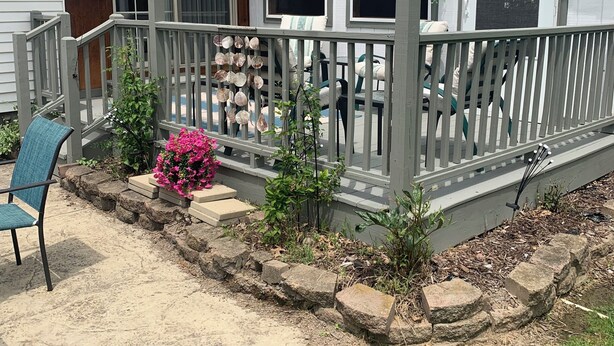 Een overdekt terras met een leuning, een stoel en een kleine tuin met planten en een roze bloem.