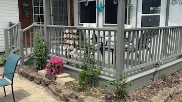 A covered porch with a railing, a chair, and a small garden area with plants and a pink flower.