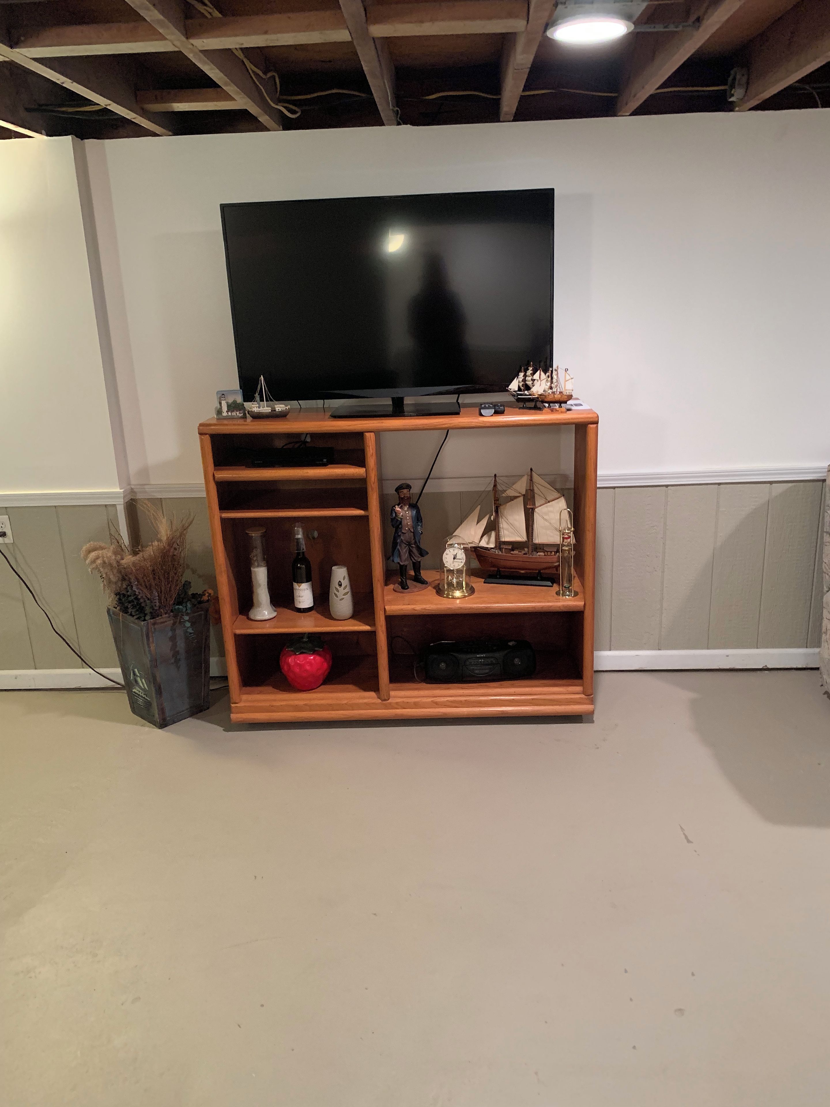 Un mueble de madera con unidad de entretenimiento, televisor de pantalla plana, repisas con adornos y un jarrón con plantas secas.