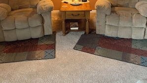 Een woonkamer met twee fauteuils, een klein houten bijzettafeltje met een lamp, een vloerkleed en een schilderij aan de muur.