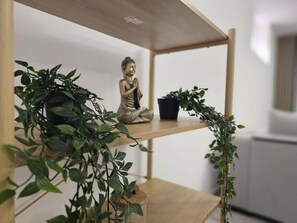 Hyllyllä on Buddha-patsas, ruukussa oleva kasvi ja pieni musta ruukku.