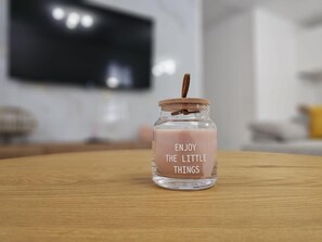 En genomskinlig glasburk med ett korklock och en etikett med texten ”NJUT AV DE SMÅ SAKERNA” placerad på en träyta.