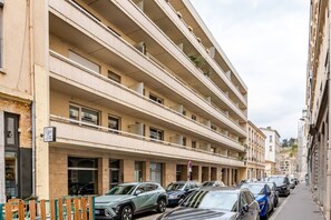 A multi-story building with balconies, parked cars, and a sign indicating a business on the ground floor. - 2-room apartment - exceptional terrace – Heart of the Presqu'île (Lyon)